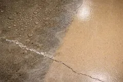 Cracked bare concrete beaded with condensation next to a freshly coated section of floor