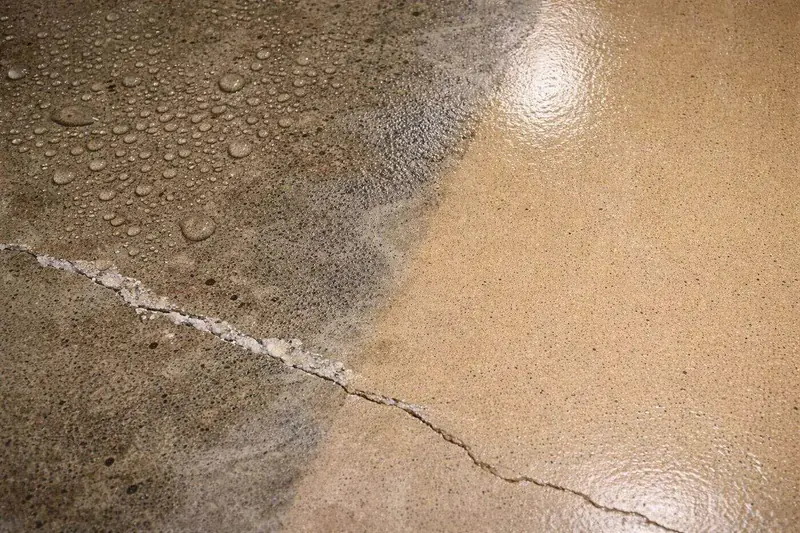 Cracked bare concrete beaded with condensation next to a freshly coated section of floor